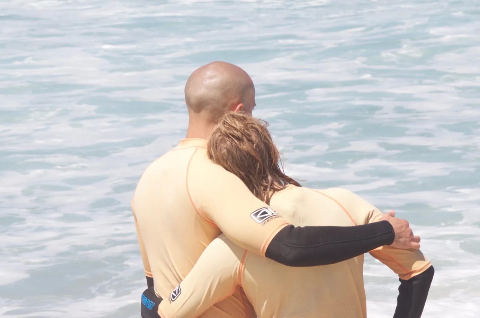 Anne and David hugging by the sea after surfing.
