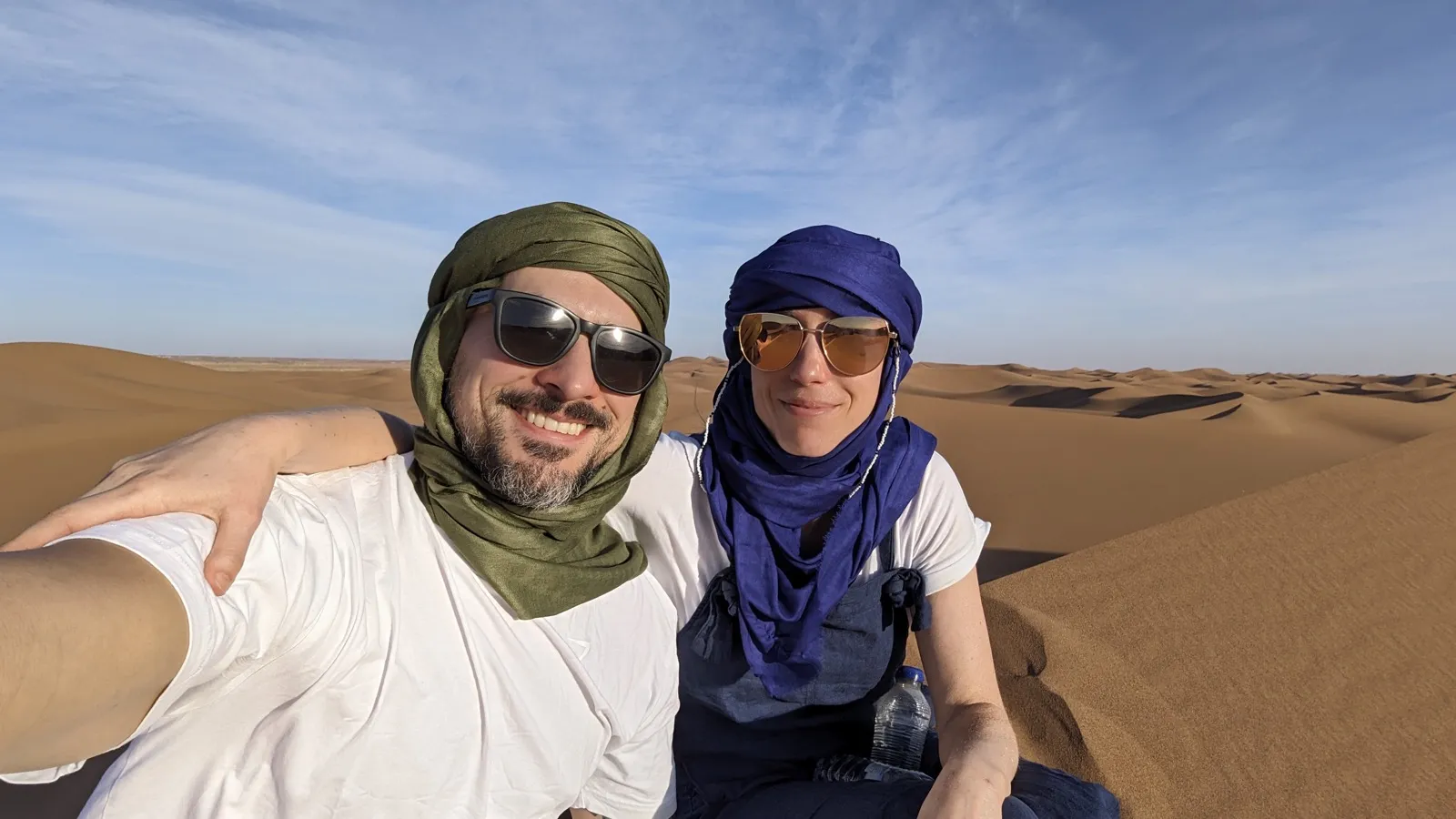 Anne and David in desert scarves, smiling on the dunes.