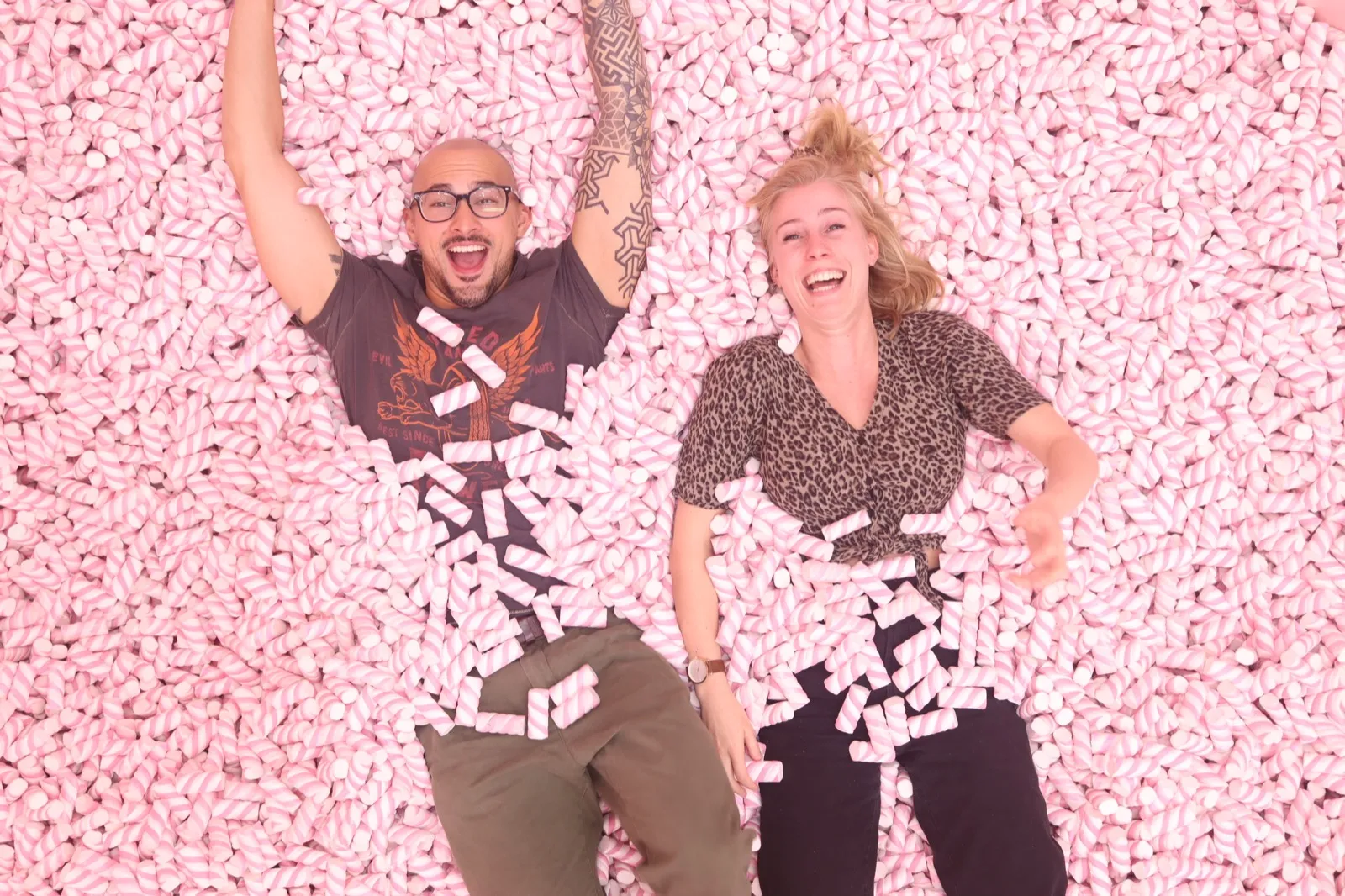 Anne and David laughing in a giant pool of pink marshmallows.