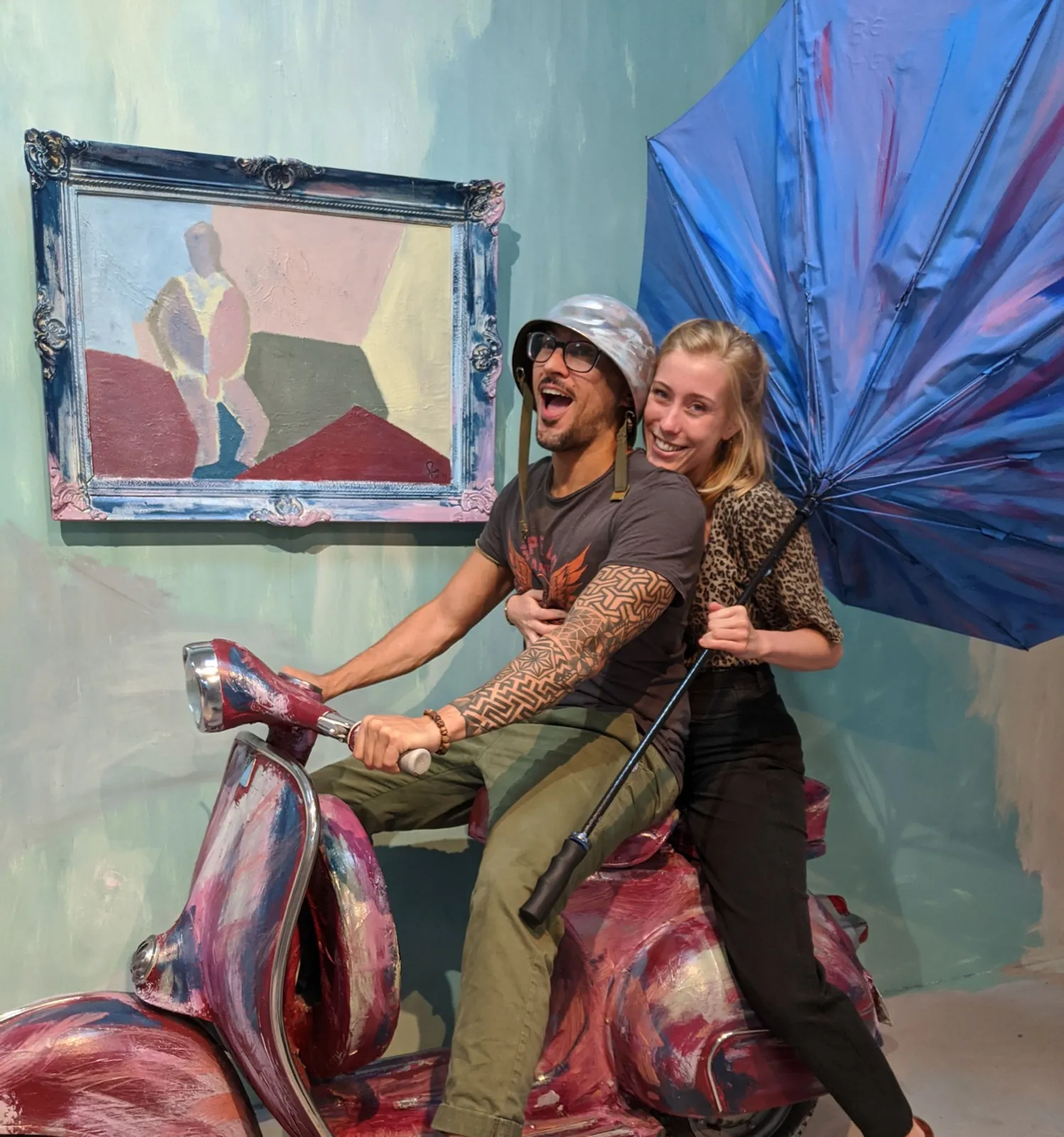 Anne and David laughing on a painted scooter with an umbrella.